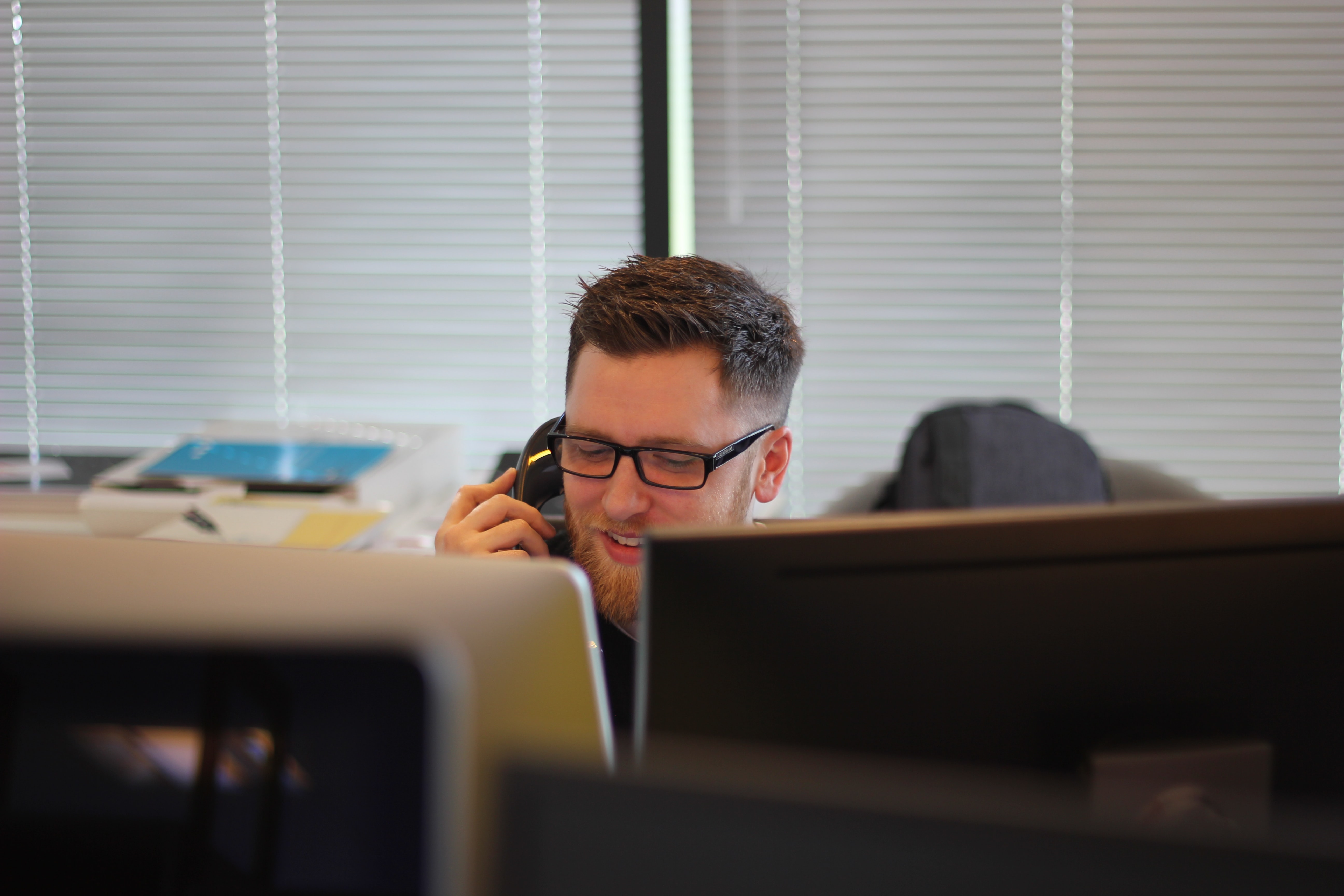 A guy talking on a phone by the desk and computers