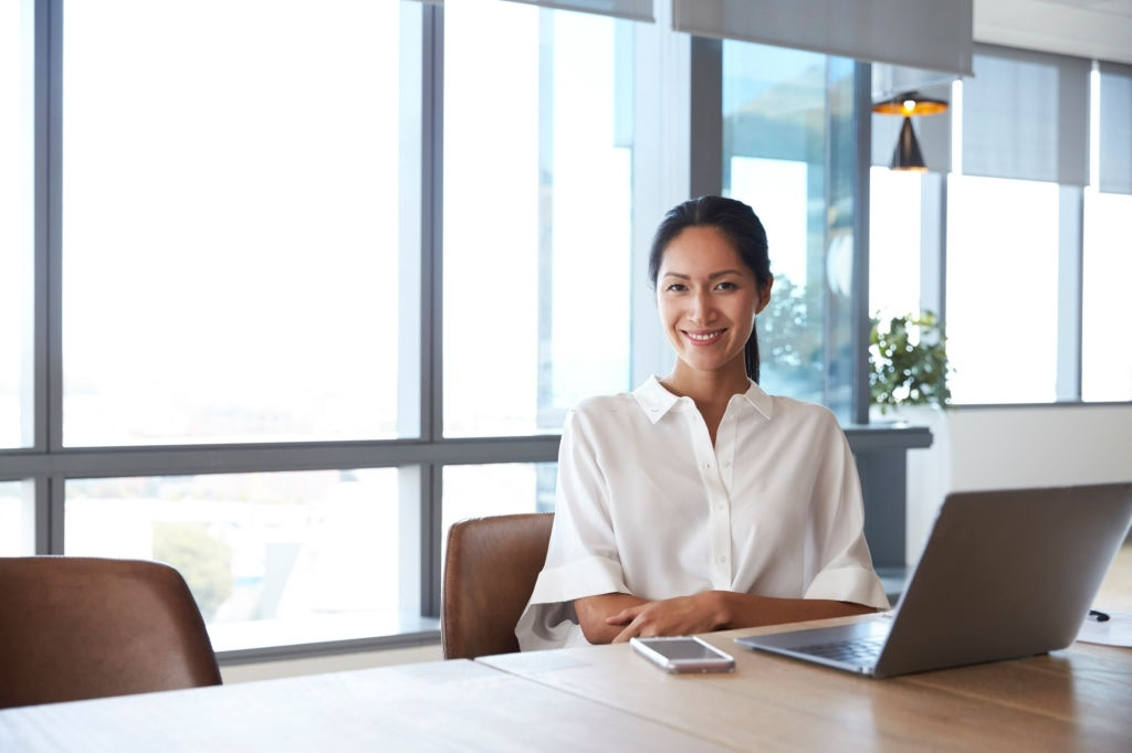 A professional woman sitting by an office desk and laptop smiling