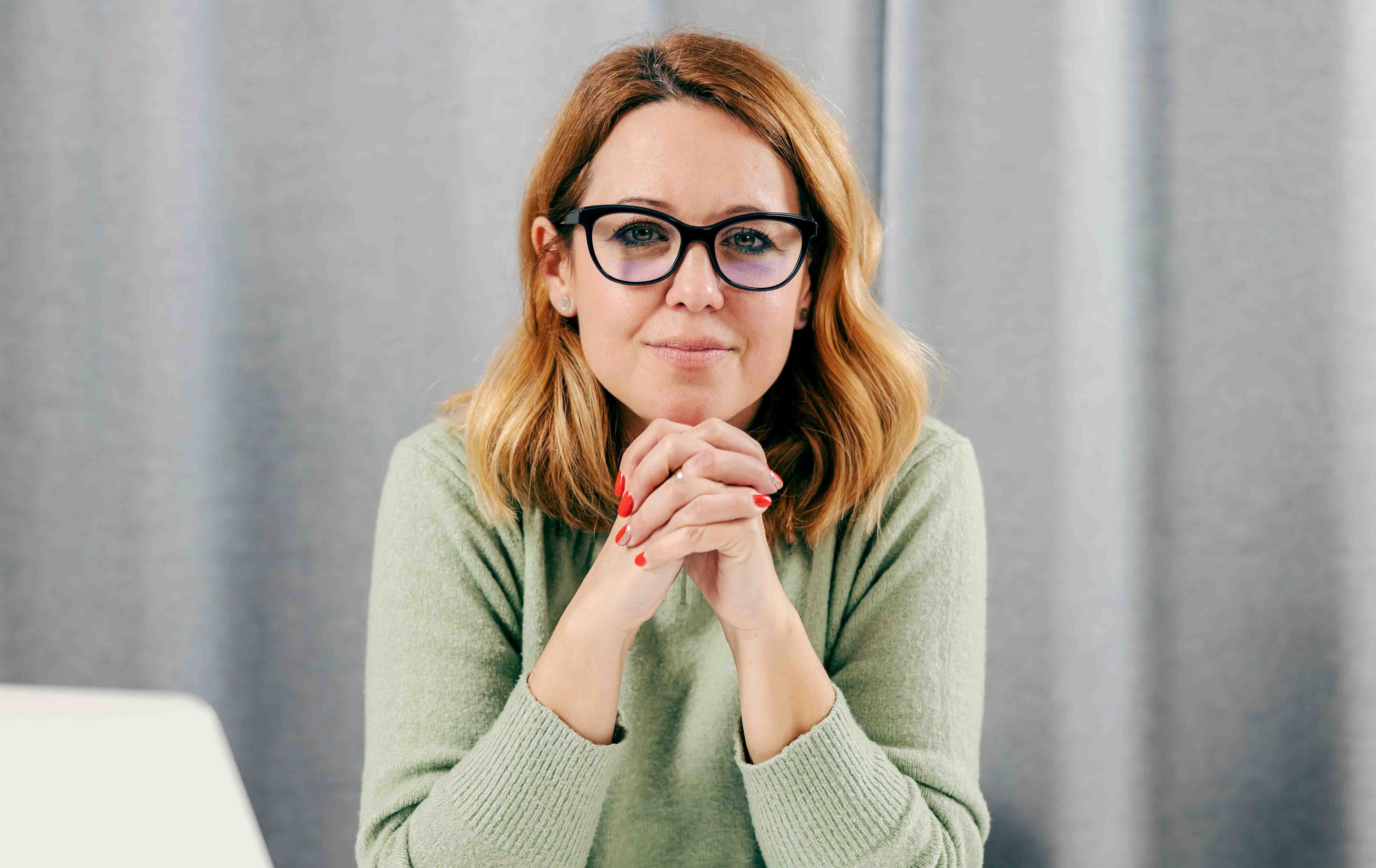 A lady wearing glass sitting by a table with hand acrossed