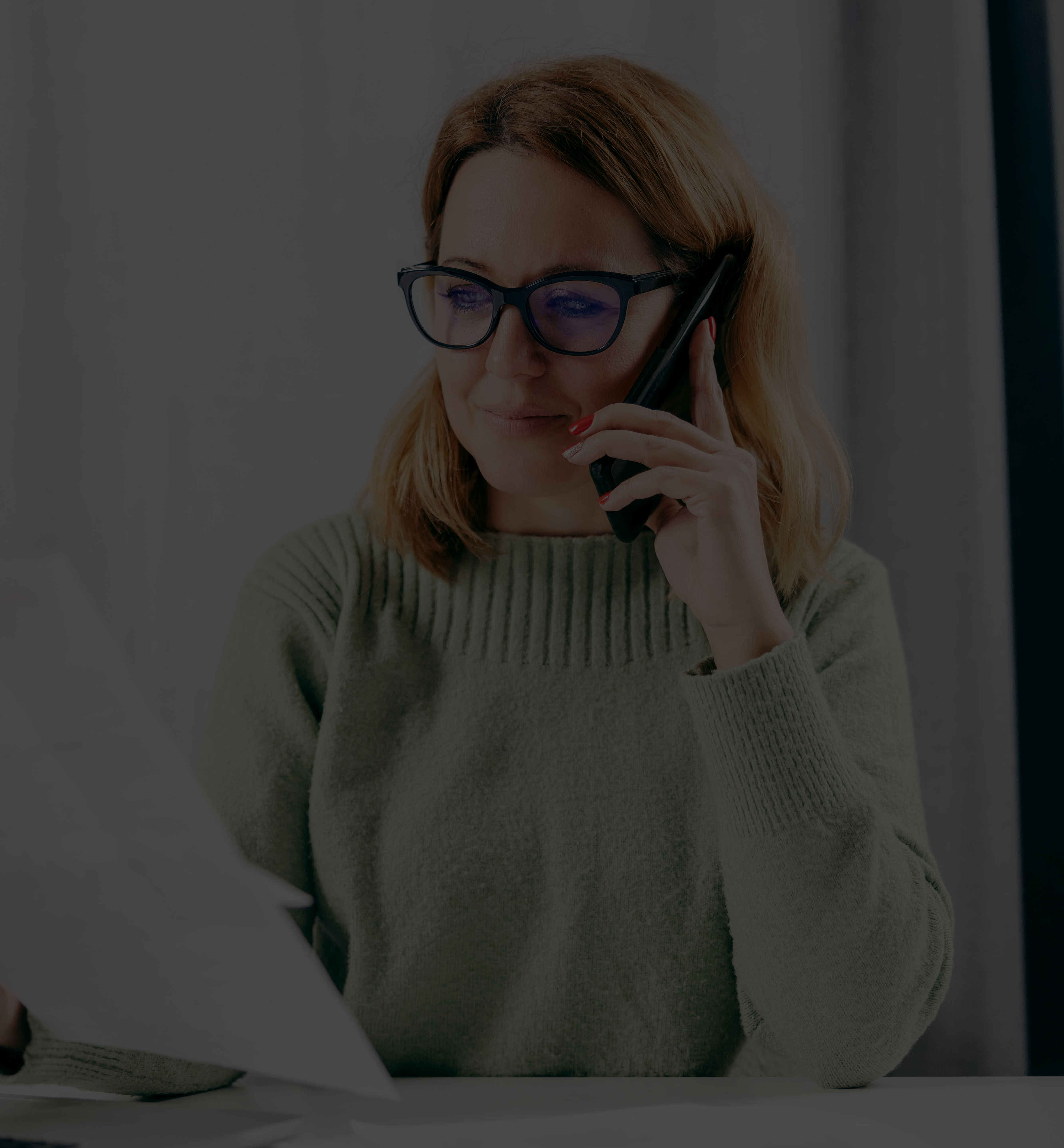 A lady wearing a pair of glasses talking on a phone with a paper in her hand 