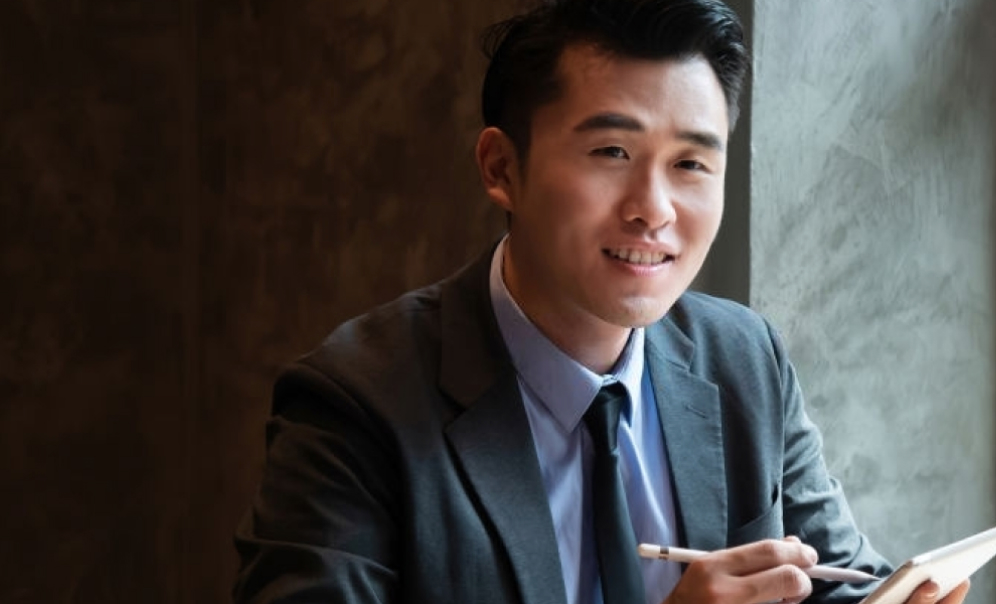 A man holding a pen and a notebook sitting on a chair