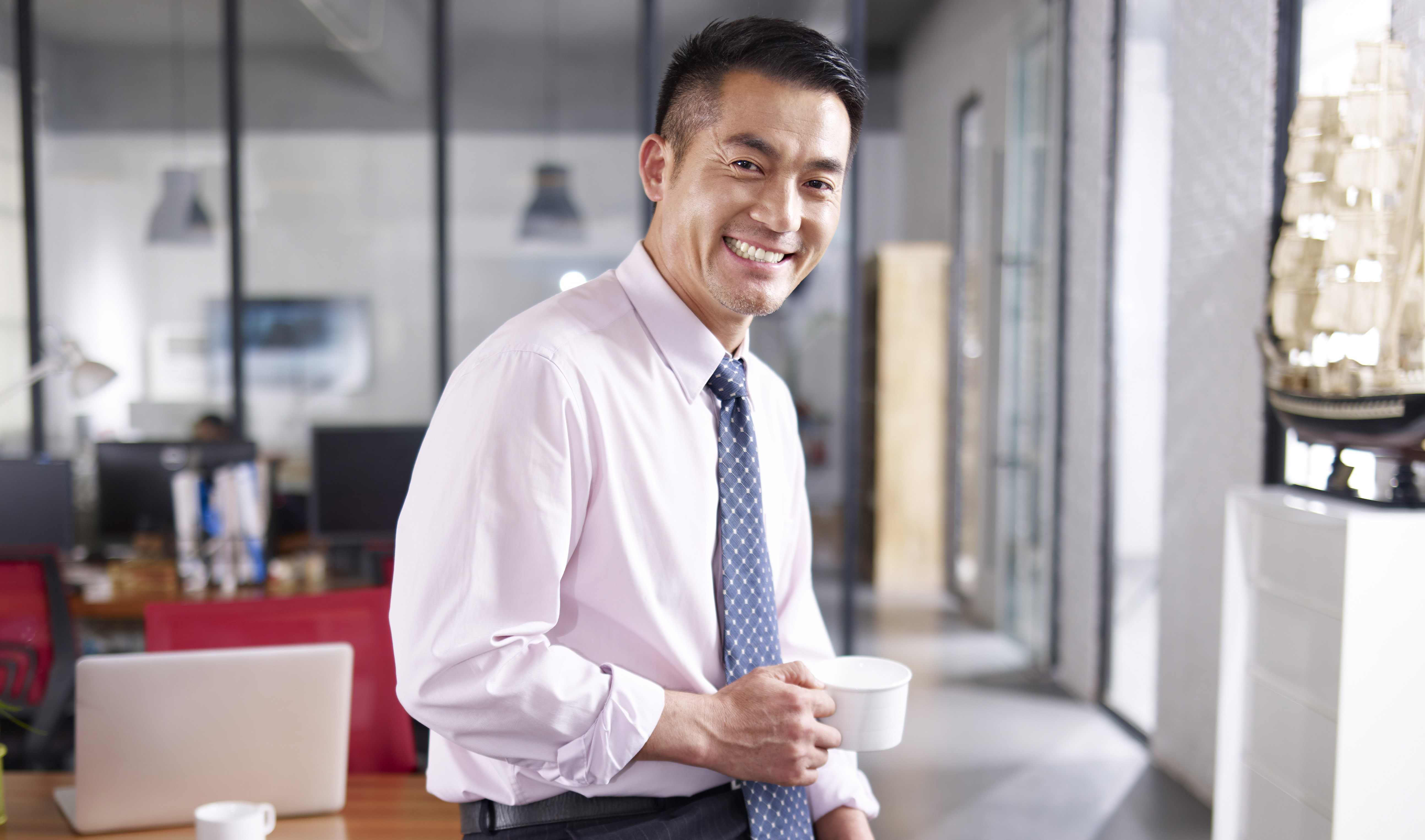 A business man sitting on an office table holding a coffee cup